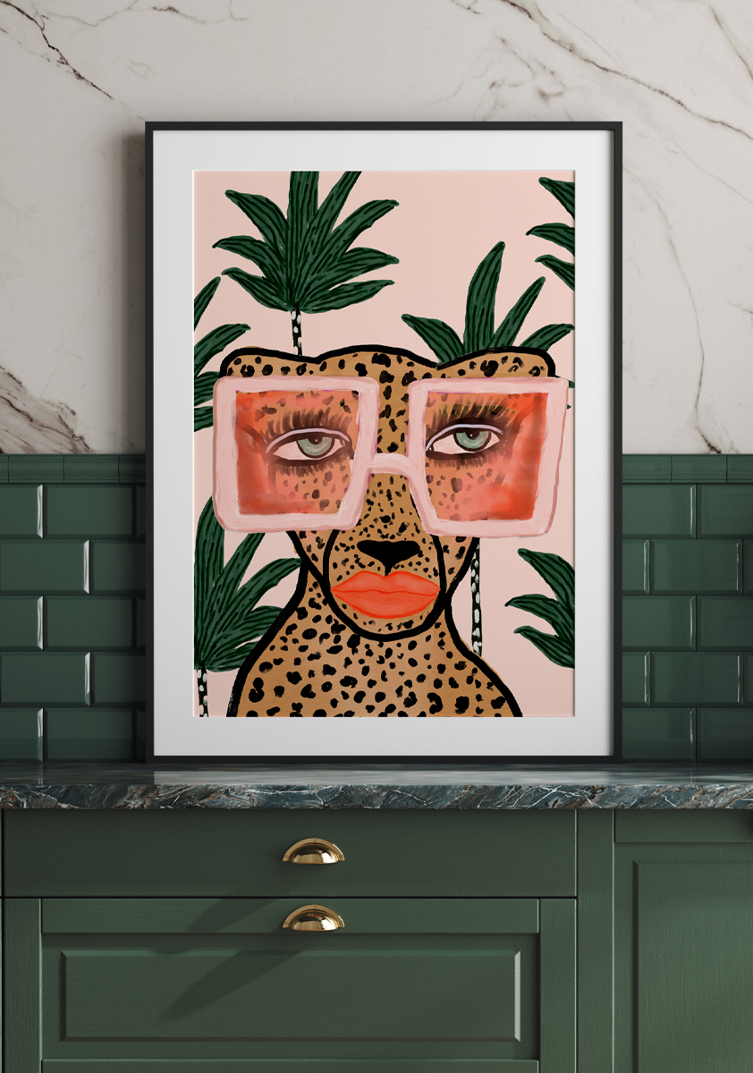 'Tropical Glam Cheetah' from Bouffants and Broken Hearts by Kendra Dandy is a portrait of a sassy cheetah wearing sunglasses and red lipstick, against a pink and green leafy background, displayed in a dark green kitchen